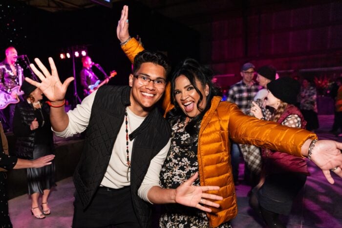 Two people in puffy jackets smile broadly at the camera from the dance floor
