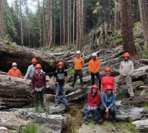 10 apprentices from 2022 Apprenticeship program standing outdoors in a forest with hardhats on